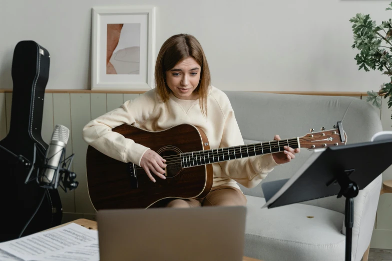 a woman sitting on a couch playing a guitar, trending on pexels, sitting at a computer, nerdy music teacher with phd, lachlan bailey, fine detailing