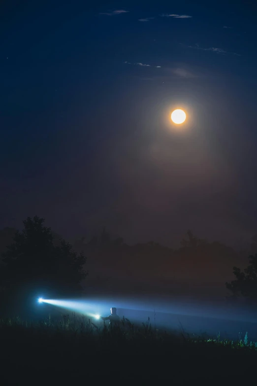 a car driving through a foggy field under a full moon, by Joe Stefanelli, lightshow, laser beam ; outdoor, dramatic lightin