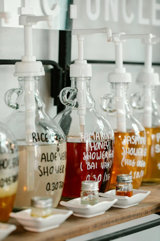 a row of bottles filled with liquid sitting on top of a counter, by Jessie Algie, unsplash, process art, maple syrup, in white lettering, radiolaria, ingredients on the table