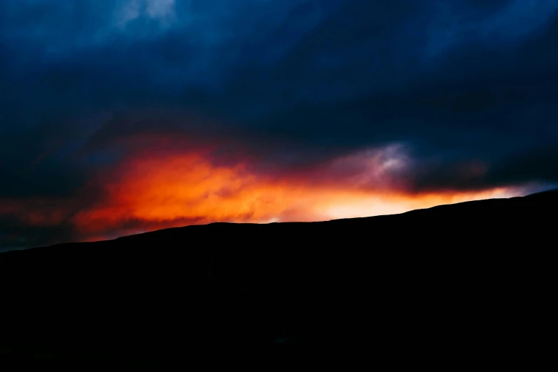 a silhouette of a person standing on top of a hill under a cloudy sky, an album cover, unsplash, hurufiyya, dark blue + dark orange, red and obsidian neon, skye meaker, sunset panorama