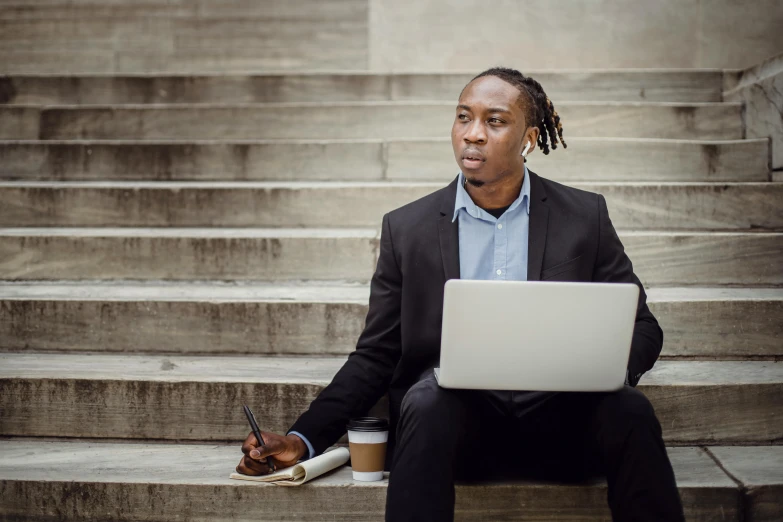 a man sitting on some steps with a laptop, pexels contest winner, man is with black skin, serious business, avatar image, holding notebook