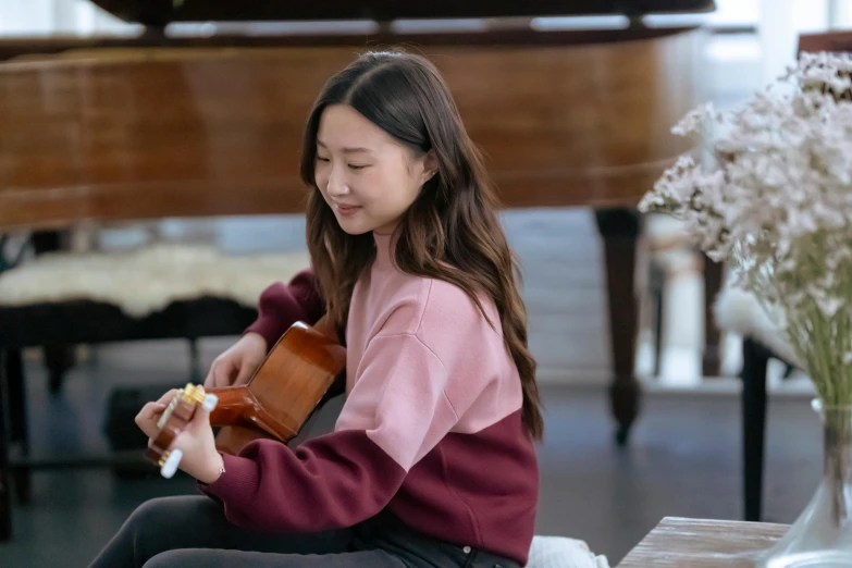 a woman sitting on a couch playing a guitar, inspired by Song Xu, happening, wearing a pastel pink hoodie, student, joy ang, delightful surroundings