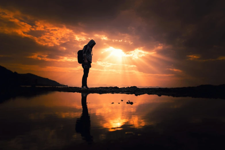 a person standing on a beach at sunset, pexels contest winner, reflective light, traveller, dramatic backgroung, praying at the sun