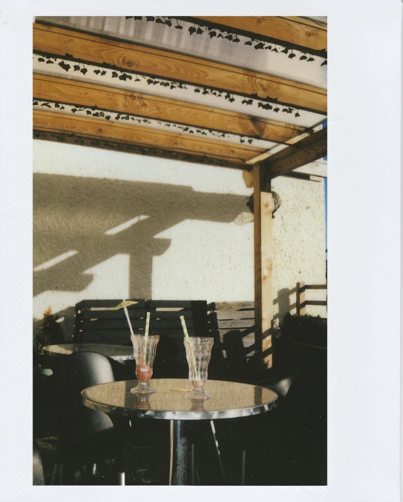 a couple of glasses sitting on top of a table, a polaroid photo, un restaurant avec une terrasse, trending on vsco, shadow polaroid photo, color photo