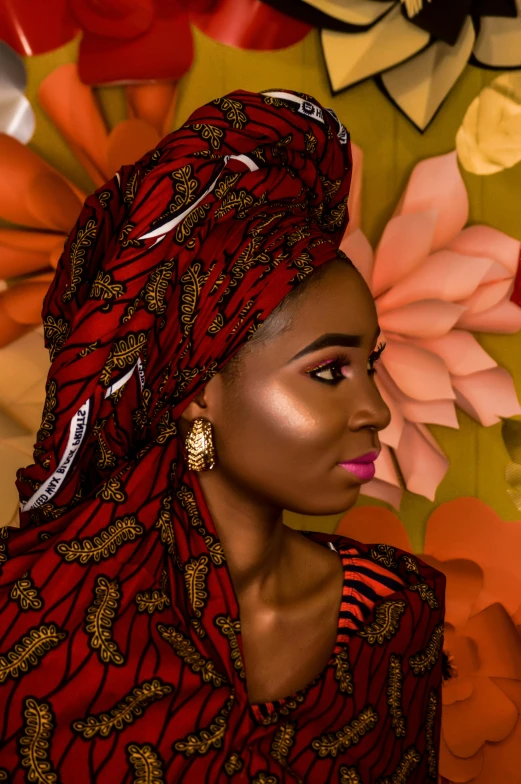 a woman standing in front of a wall with flowers, inspired by Chinwe Chukwuogo-Roy, trending on pexels, afrofuturism, red silk scarf, somali attire, close - up studio photo, vibrant lights