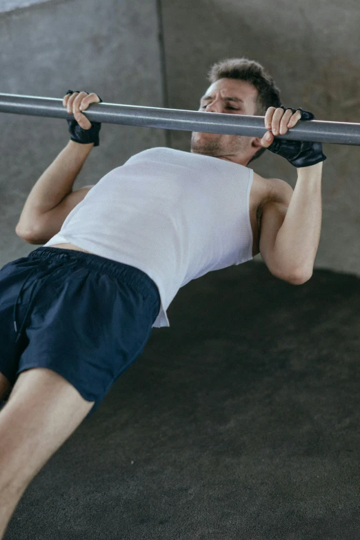 a man is doing a pull up on a bar, sport bra and dark blue shorts, laying down with wrists together, #trending, commercial