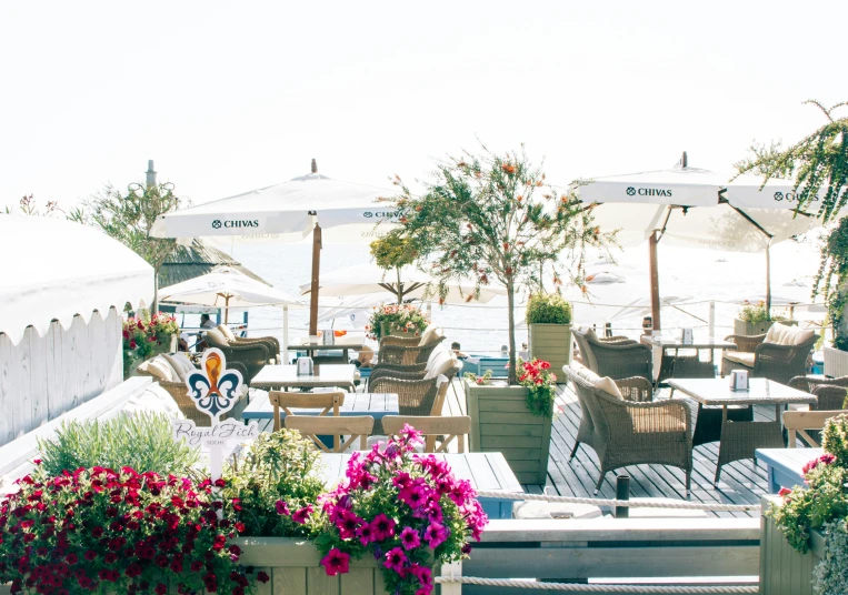 a patio area with tables, chairs and umbrellas, unsplash, sea cloud, sitting with flowers, hollywood standard, at the waterside