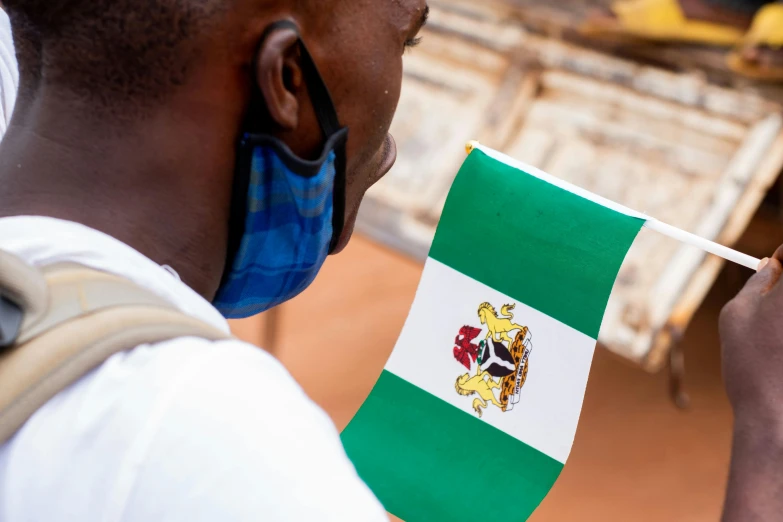 a man in a face mask holding a flag, an album cover, by Chinwe Chukwuogo-Roy, pexels contest winner, symbolism, green flag, praying, on a canva, zoomed in