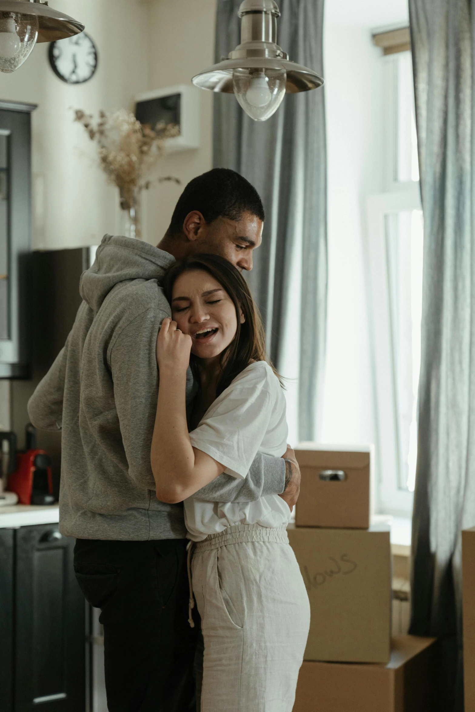 a woman hugging a man in a kitchen, pexels contest winner, happening, in a living room, happy girl, moving, black haired girl wearing hoodie