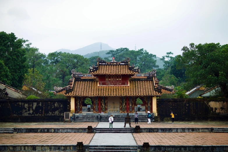 a group of people standing in front of a building, inspired by Gu An, unsplash contest winner, vietnamese temple scene, square, a park, brown