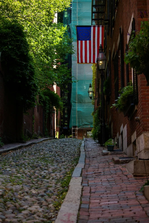 a narrow cobblestone street with a clock tower in the background, by Brian Alfred, unsplash contest winner, boston celtics, american flags, humid evening, shady alleys