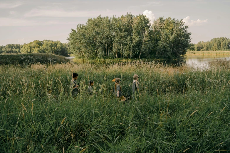 a group of people standing on top of a lush green field, by Attila Meszlenyi, unsplash, land art, tall grown reed on riverbank, kids playing, dwell, school