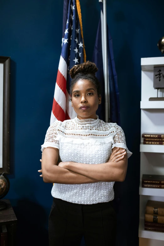 a woman standing in front of an american flag, a portrait, dark-skinned, in office, promotional still, alana fletcher