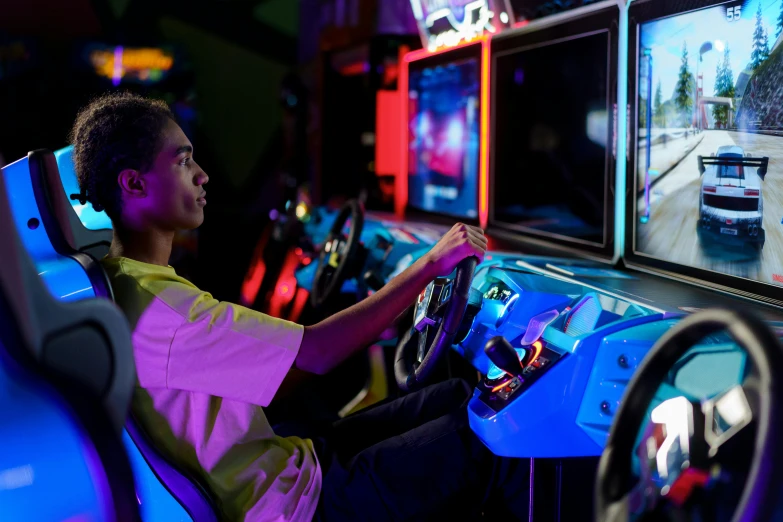 a young man is playing a video game, pexels, interactive art, alien racing drivers, pink yellow and blue neon signs, low fi, initial d