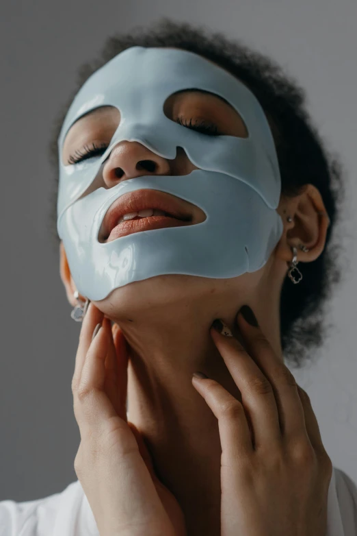 a woman with a sheet mask on her face, an album cover, trending on pexels, blue gray, silicone skin, glossy, grey