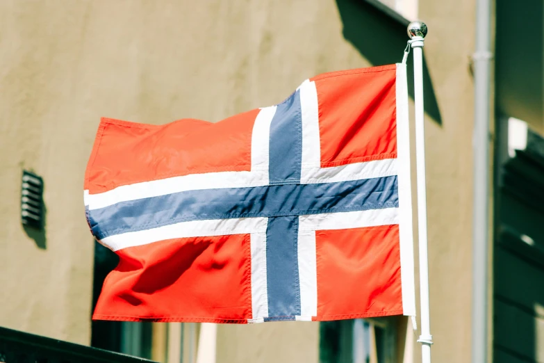 a flag on a pole in front of a building, by Jesper Knudsen, unsplash, hurufiyya, norwegian, slightly tanned, crypto, seen from the side