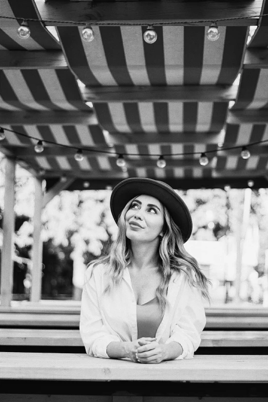 a woman in a hat sitting on a bench, a black and white photo, by Julia Pishtar, smiling down from above, casey cooke, sydney sweeney, looking up to the sky