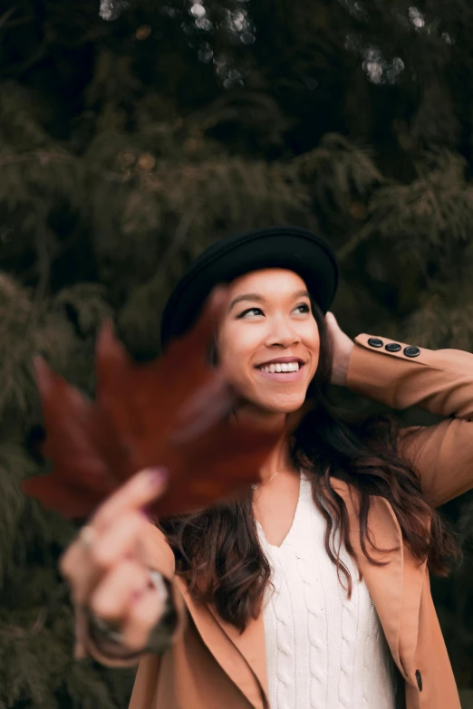 a woman holding a leaf in front of her face, trending on pexels, caracter with brown hat, half asian, smiling down from above, avatar image