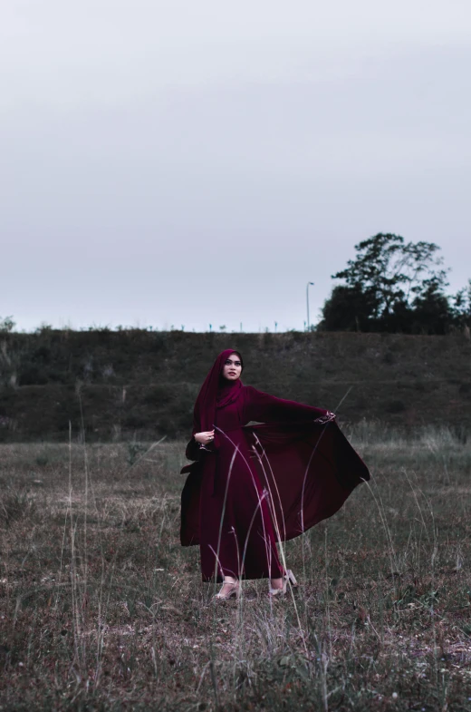 a woman in a red cloak standing in a field, an album cover, by Ismail Acar, pexels contest winner, hurufiyya, dark purple garments, full body with costume, show, casual pose