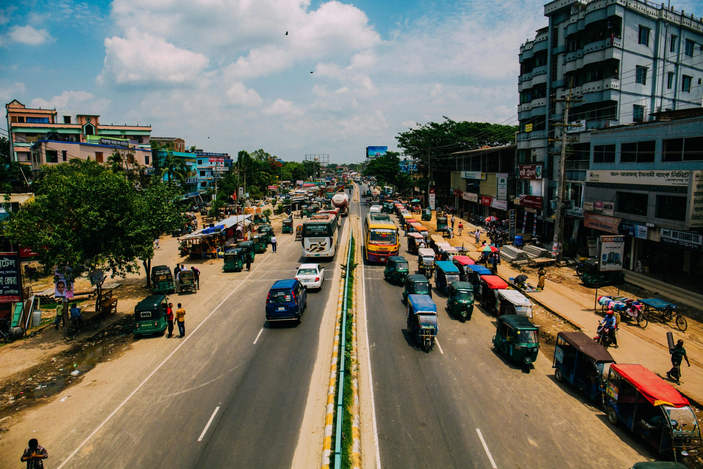 a street filled with lots of traffic next to tall buildings, unsplash, hurufiyya, assam tea village background, buses, thumbnail, street of teal stone