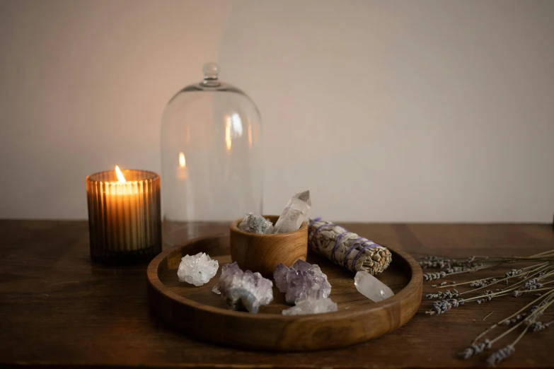 a candle sitting on top of a wooden table next to a glass clochet, by Helen Stevenson, unsplash, amethyst mineral quartz, on a wooden tray, glass domes, soft light misty
