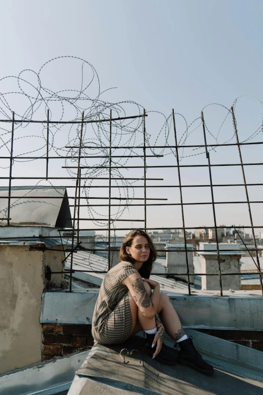 a woman sitting on the roof of a building, a tattoo, inspired by Elsa Bleda, pexels contest winner, graffiti, barbed wire, ukraine. photography, prison bars, low quality photo