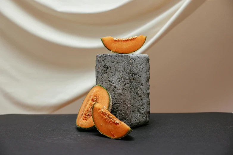 a piece of melon sitting on top of a block of concrete, a still life, unsplash, background image, smoky, miniature product photo, grey orange