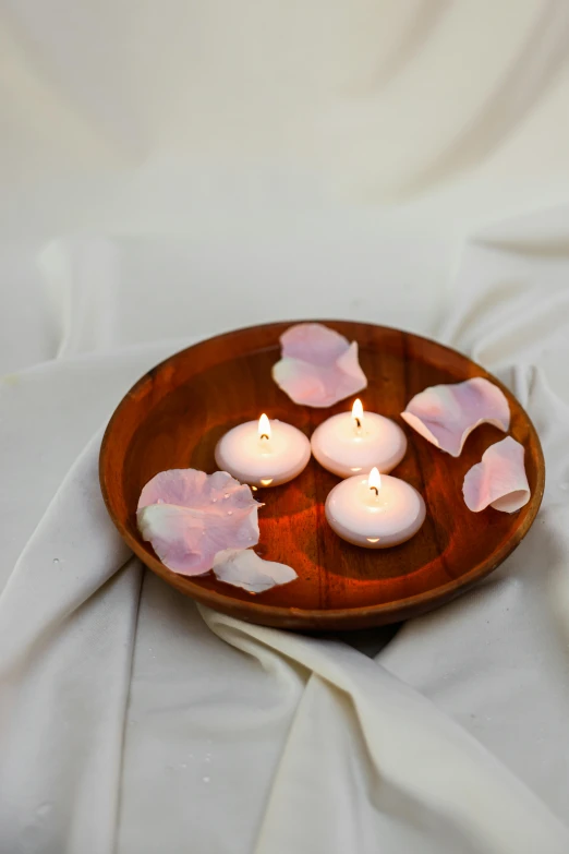 a wooden plate topped with candles on top of a white cloth, pink petals, full product shot, modeled, float