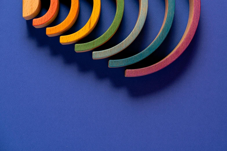 a group of wooden toys sitting on top of a blue surface, op art, arcs, complementary colour scheme, moonbow, detailed product shot