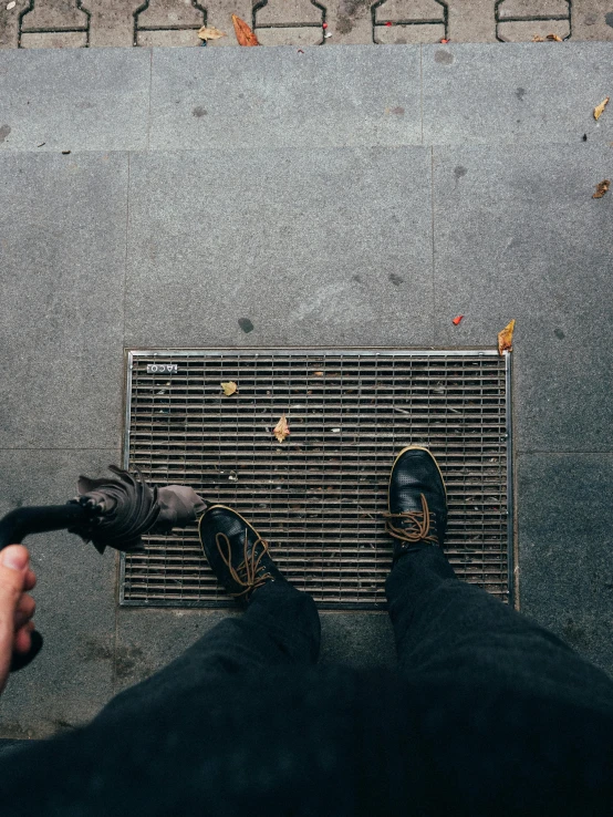 a person standing on a sidewalk holding an umbrella, pexels contest winner, realism, sewage falling from grates, holding a wrench, trending on vsco, leaves trap