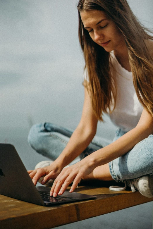 a woman sitting on a wooden table using a laptop, by Carey Morris, trending on pexels, renaissance, teenage girl, sitting on a rock, website banner, wearing casual clothing