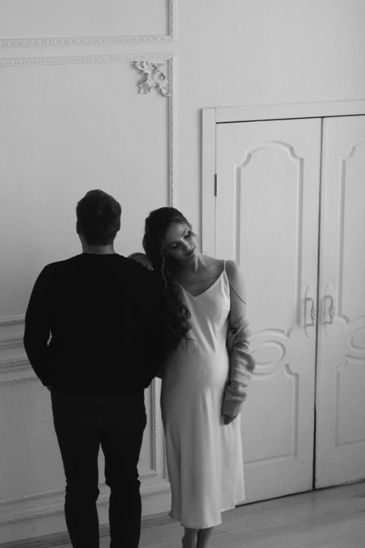 a man and a woman standing next to each other, a black and white photo, by Alexis Grimou, romanticism, editorial footage, leaving a room, yulia nevskaya, wearing long gown