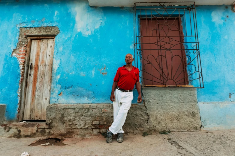 a man standing in front of a blue building, an album cover, inspired by Steve McCurry, pexels contest winner, renaissance, cuban revolution, red and blue garments, in front of the house, 15081959 21121991 01012000 4k