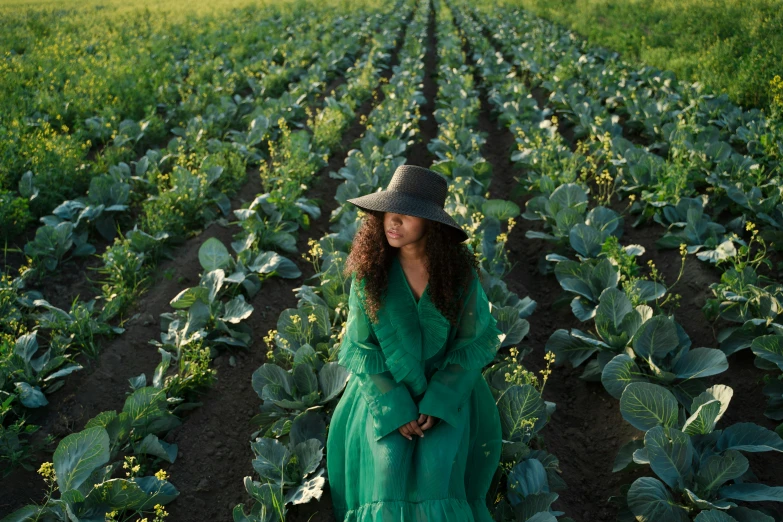 a woman in a green dress standing in a field, an album cover, inspired by Gordon Parks, pexels contest winner, renaissance, rows of lush crops, green hat, imaan hammam, anna nikonova