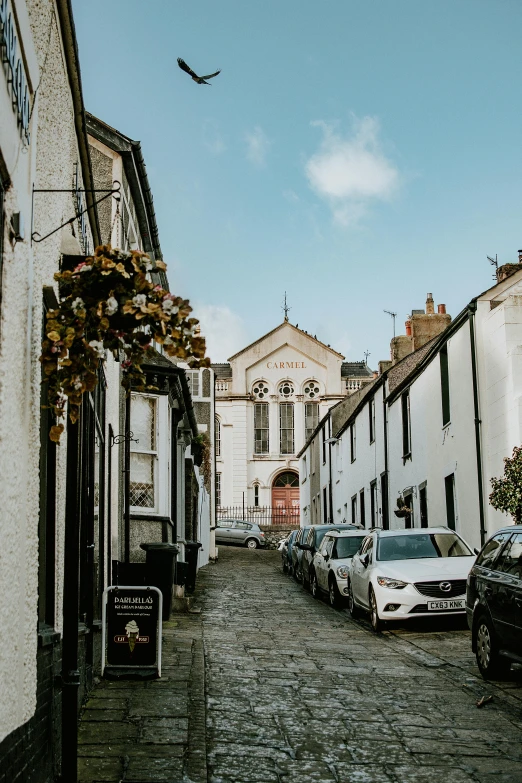 a narrow cobblestone street lined with parked cars, by Kev Walker, pexels contest winner, arts and crafts movement, white church background, maryport, unsplash photography, upon a peak in darien