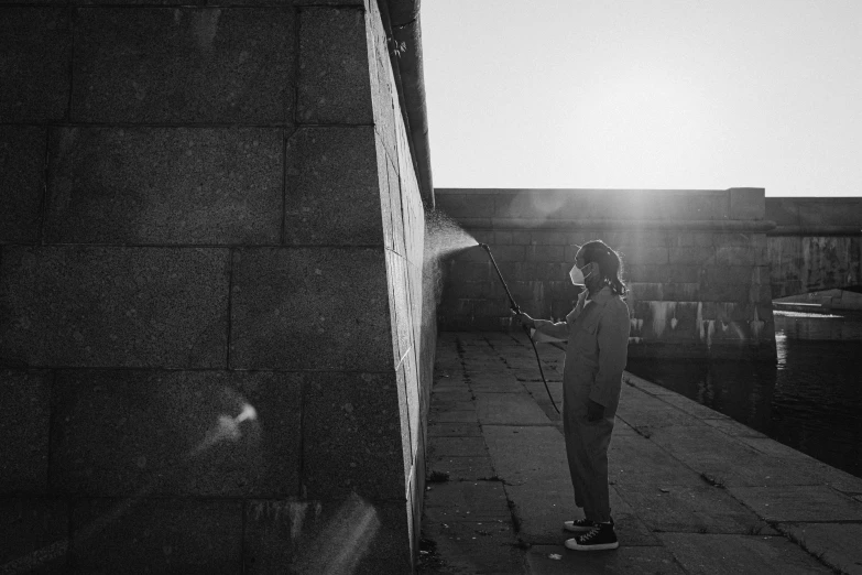 a black and white photo of a person standing on a sidewalk, a black and white photo, by Jan Kupecký, unsplash, graffiti, the girl and the sun, cleaning future, on rooftop, spraying liquid