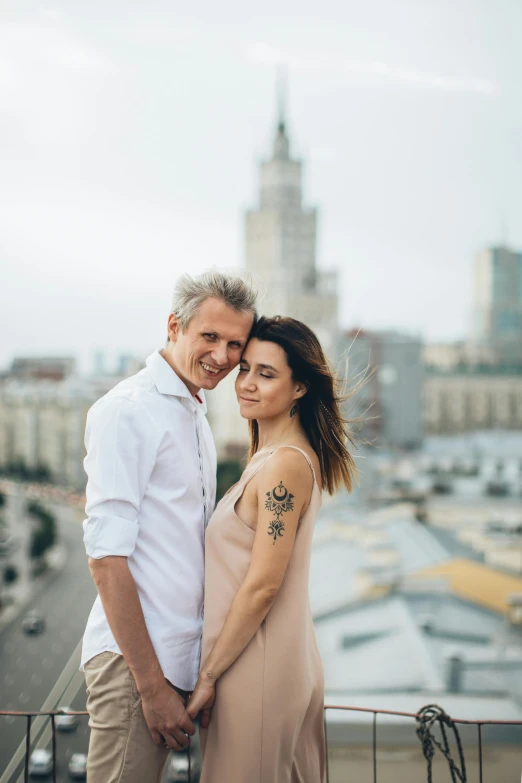 a man and woman standing next to each other on a balcony, by Adam Marczyński, pexels contest winner, skyscrapers in the background, kremlin, lovingly looking at camera, square