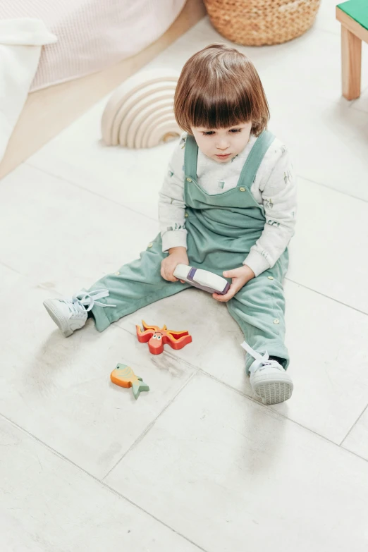 a little girl sitting on the floor playing with toys, by Andries Stock, pexels, holding a very advance phone, soft cracks, wearing overalls, stand on stone floor