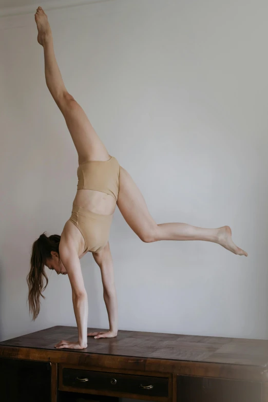 a woman doing a handstand on top of a table, inspired by Elizabeth Polunin, unsplash, arabesque, low quality photo, bodysuit, sydney hanson, pale skin