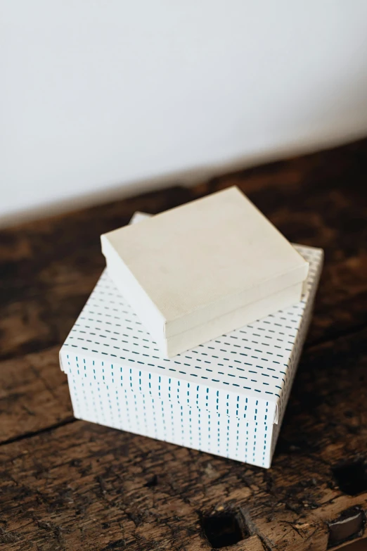 a stack of white boxes sitting on top of a wooden table, an album cover, by Rebecca Horn, unsplash, delicate patterned, soap, dot, indigo