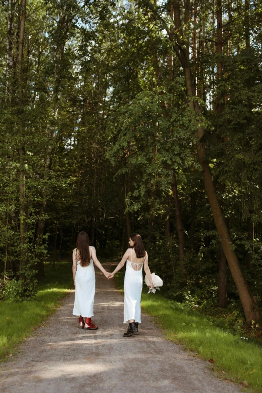 a couple of women walking down a dirt road, an album cover, by Julia Pishtar, unsplash, renaissance, wearing white cloths, forest backdrop, holding hands, ukraine. photography