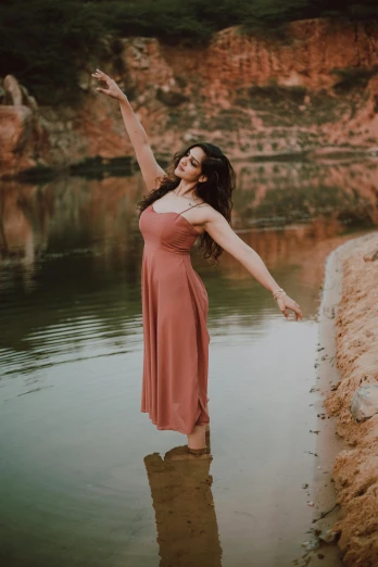 a woman in a dress is standing in the water, pexels contest winner, arabesque, satisfied pose, warm muted colors, near pond, doing a sassy pose