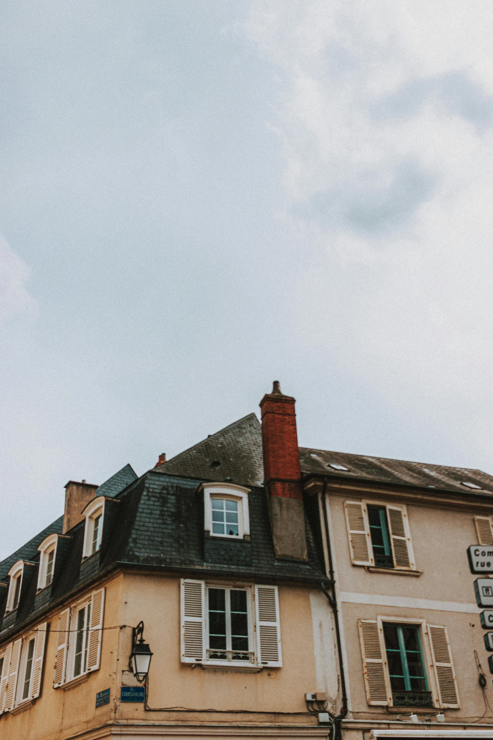 a tall building sitting on the side of a street, by Andrée Ruellan, unsplash, french village interior, simple gable roofs, smokey chimney, trending on vsco