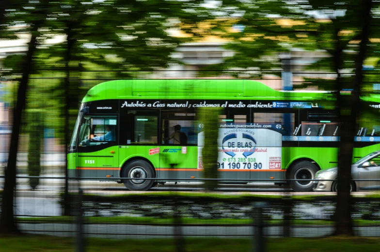 a green bus driving down a street next to trees, a picture, fast energy, advertising photo, fan favorite, unblur