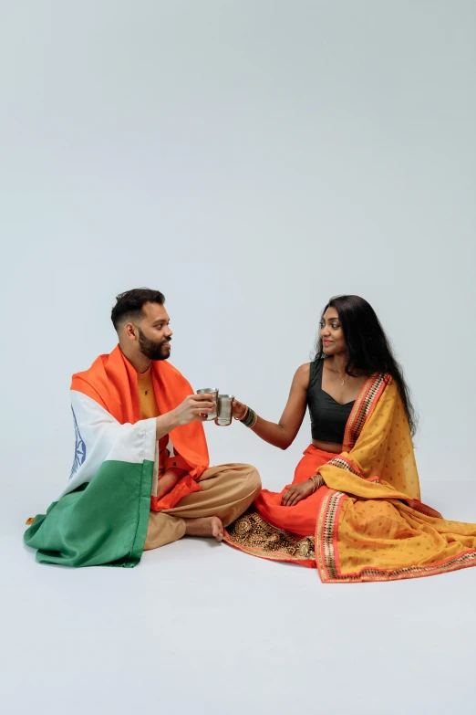 a man and a woman sitting next to each other, hurufiyya, indian flag, diverse outfits, celebration of coffee products, reaching out to each other