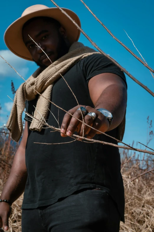 a man in a hat and scarf standing in a field, pexels contest winner, land art, man is with black skin, hand holding a knife, willow plant, cotton