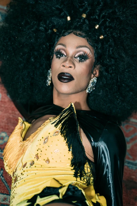 a woman with a big afro sitting on a couch, an album cover, trending on pexels, renaissance, ru paul\'s drag race, black and yellow, emaciated black evening gown, close up half body shot