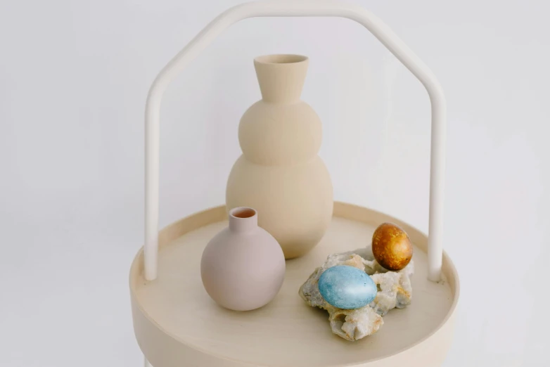 a couple of vases sitting on top of a table, a still life, unsplash, with an easter basket, sand color, japanese collection product, round-cropped