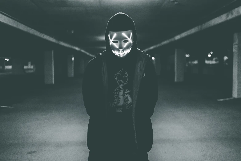 a man wearing a mask standing in a parking garage, a black and white photo, by Adam Marczyński, pexels contest winner, graffiti, white glowing eyes, black hoodie techie, horror wallpaper aesthetic, discord profile picture