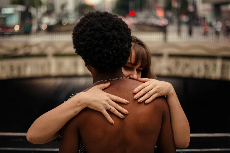 a woman hugging a man on the back of a bench, by Julia Pishtar, trending on pexels, renaissance, man is with black skin, lesbian, showing her shoulder from back, surrounding the city